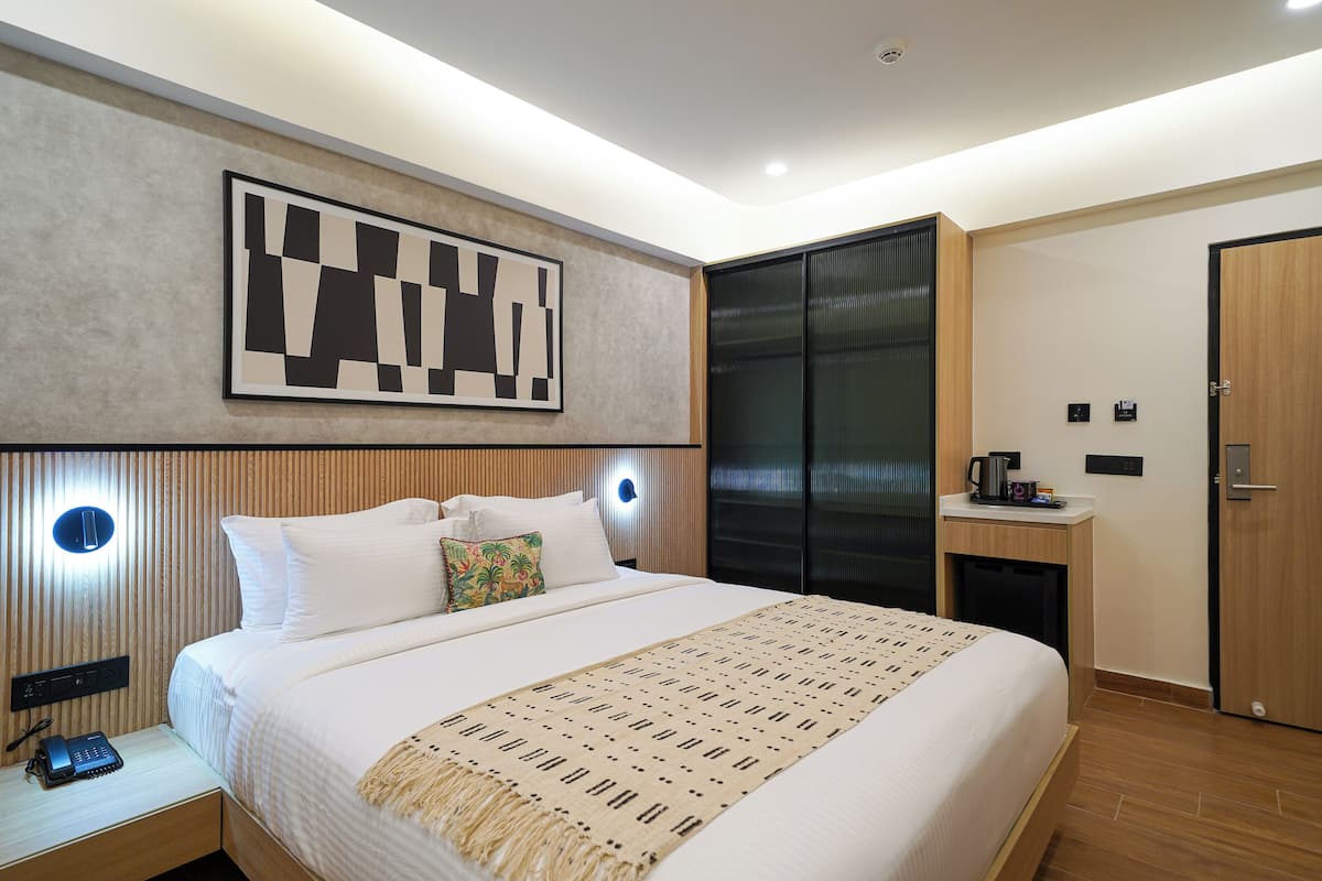 Ein modernes Hotelzimmer mit einem großen Bett, einem Nachttisch mit Telefon, einer Wandleuchte und einem großen abstrakten Gemälde.