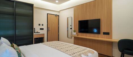 A modern hotel room with a large bed, a desk with a flat-screen TV, a mirror, and a sliding door.
