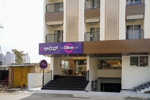 Entrada de hotel con un letrero morado, una escalera y un acceso con reja.