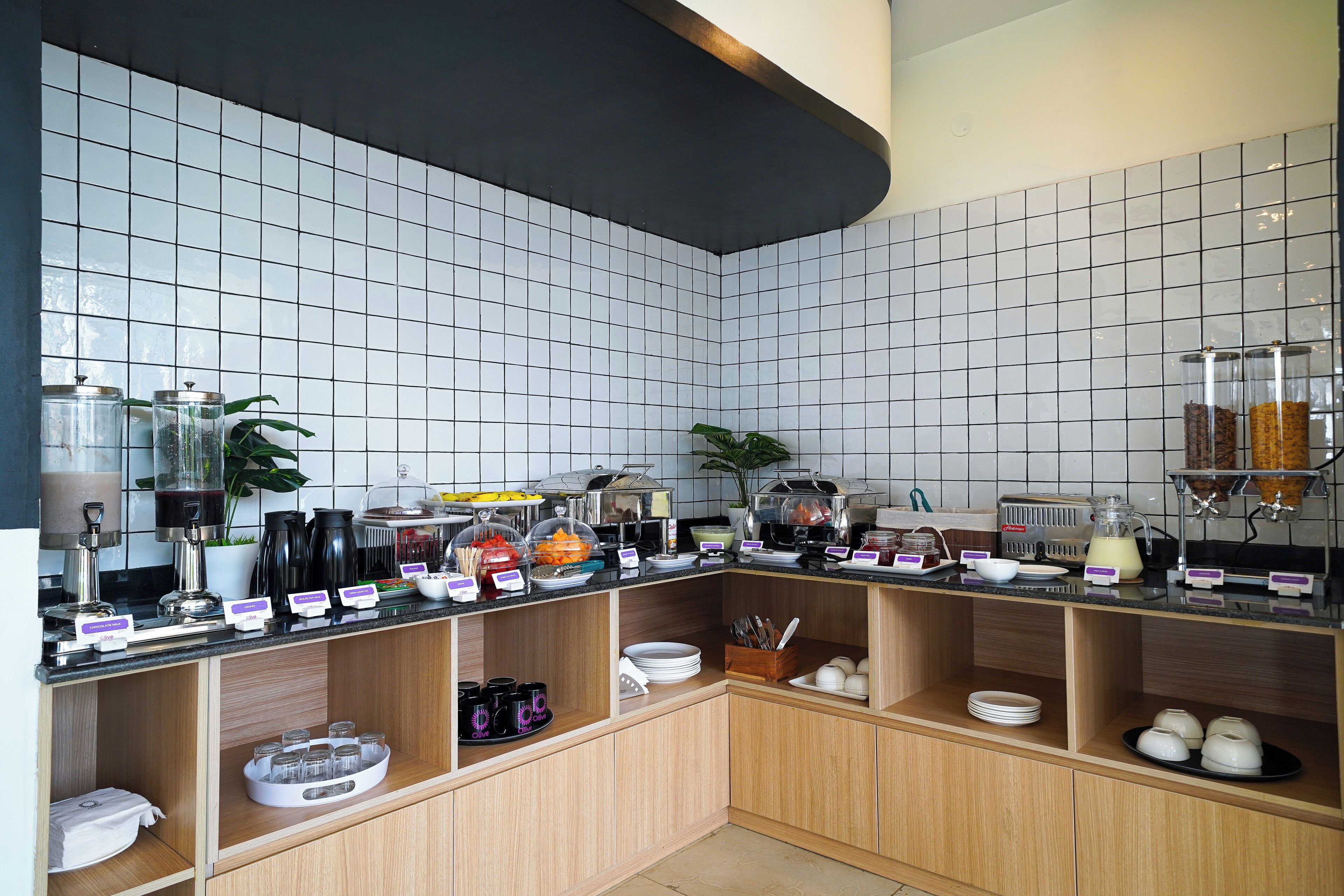 Montaje de bufé con diferentes opciones de comida y bebidas, que incluye una estación de café, barra de ensaladas y una presentación de frutas.