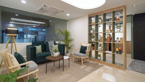 A modern living room with a green sofa, two armchairs, a coffee table, and a bookshelf filled with decorative items.