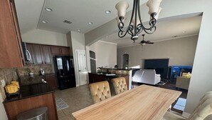 A modern kitchen with dark cabinetry, a stainless steel refrigerator, and a wooden dining table with cushioned chairs. - Cypress Moss Retreat in Legacy 4BR 2BA (Bossier City)