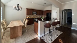 A modern kitchen with a central island, dark wood cabinets, and a dining area with a wooden table and chairs. - Cypress Moss Retreat in Legacy 4BR 2BA (Bossier City)