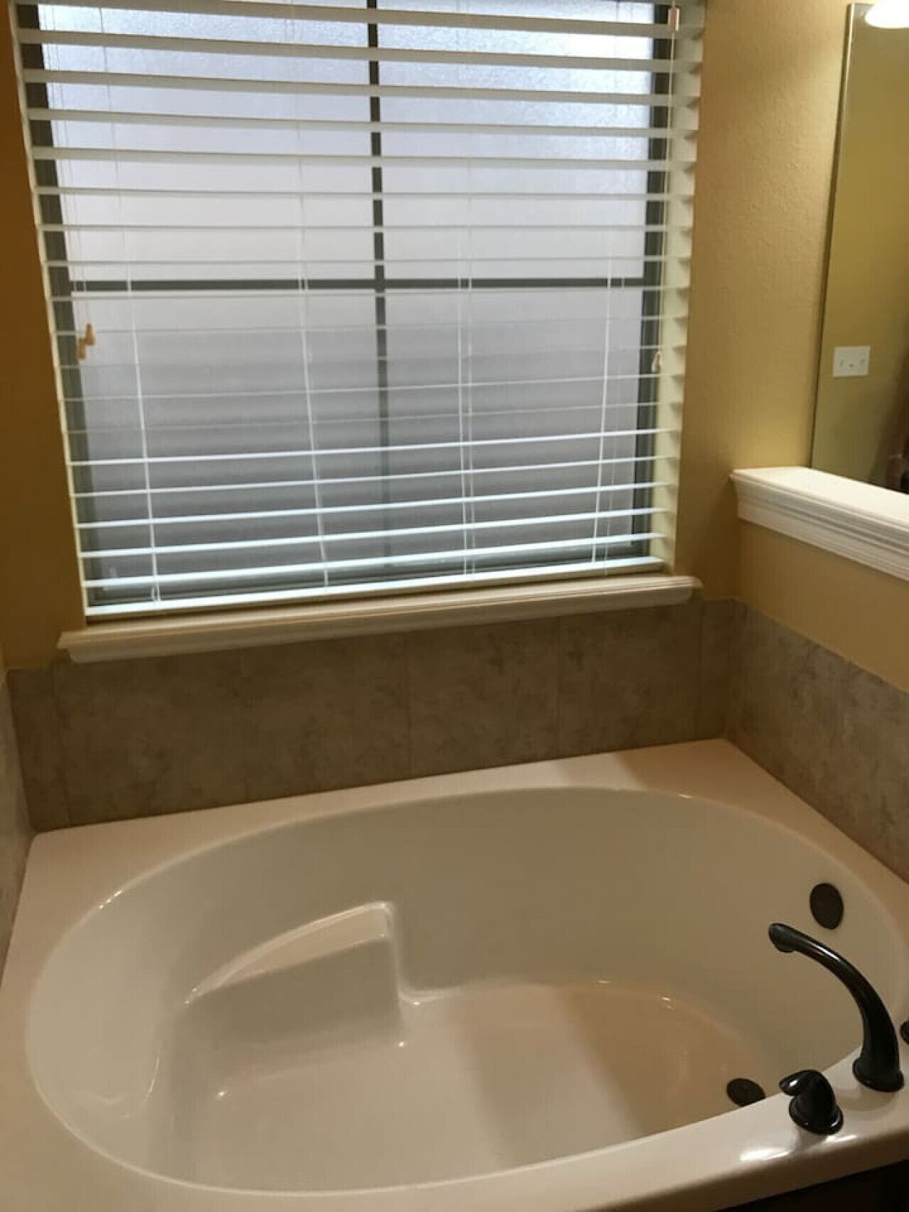 Ein Badezimmer mit einer Badewanne, einem Fenster mit Jalousien und einem Spiegel.