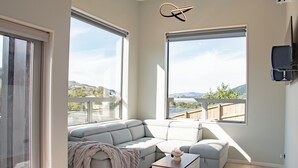 A modern living room with a sectional sofa, a coffee table, and large windows offering a view of the outdoors. - Modern Contemporary Single Detach Home (Wellington)