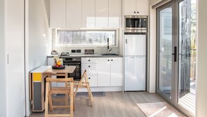 A compact kitchen with white cabinets, a built-in oven, and a microwave. There's a wooden table with chairs and a small window above the sink. - Modern Contemporary Single Detach Home (Wellington)
