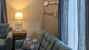 A cozy living room with a sectional sofa, a small side table with a lamp, and a wall-mounted coat rack. - Newly Renovated Acadia Apartment Maple Street (Ellsworth)