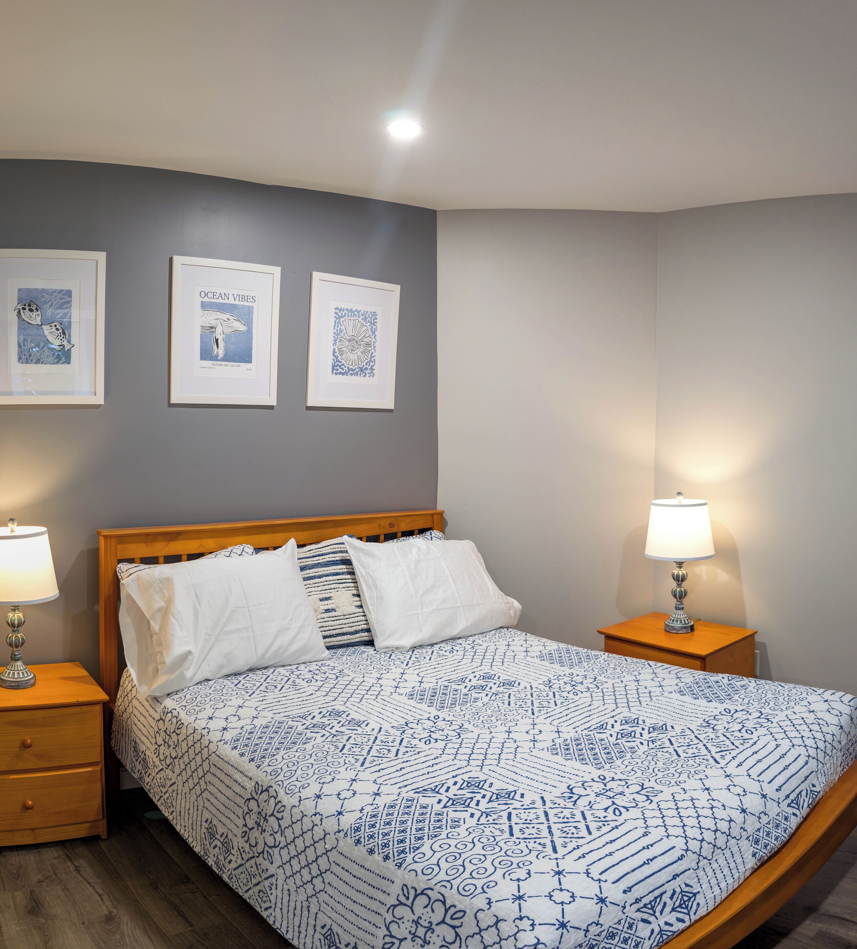 A bedroom with a bed, two bedside tables, and three framed artworks on the wall.