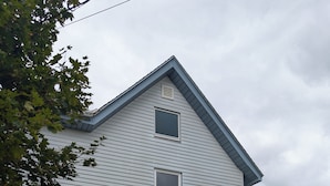 A two-story house with a blue door, a small front porch, and two well-maintained evergreen bushes. - Newly Renovated Acadia Apartment Maple Street (Ellsworth)