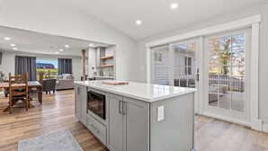 A modern kitchen with grey cabinets, a central island, and a dining area with a wooden table and chairs.