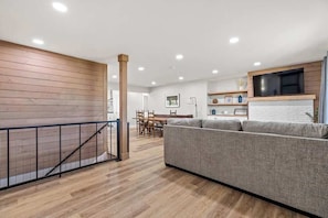 A modern living room with a grey sofa, wooden flooring, and a TV mounted on a white brick wall. - Modern Ranch in Skaneateles (Skaneateles)
