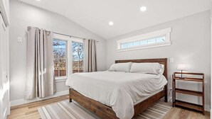A bedroom with a wooden bed, a window with curtains, a bedside table, and a nightstand.
