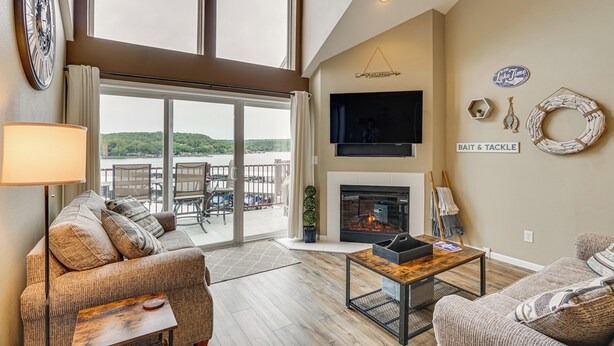 A spacious living room with a fireplace, comfortable seating, a flat-screen TV, and a view of the outdoors. - 'Lake It Easy' Waterfront Ozarks Condo w/ Balcony! (Camdenton)