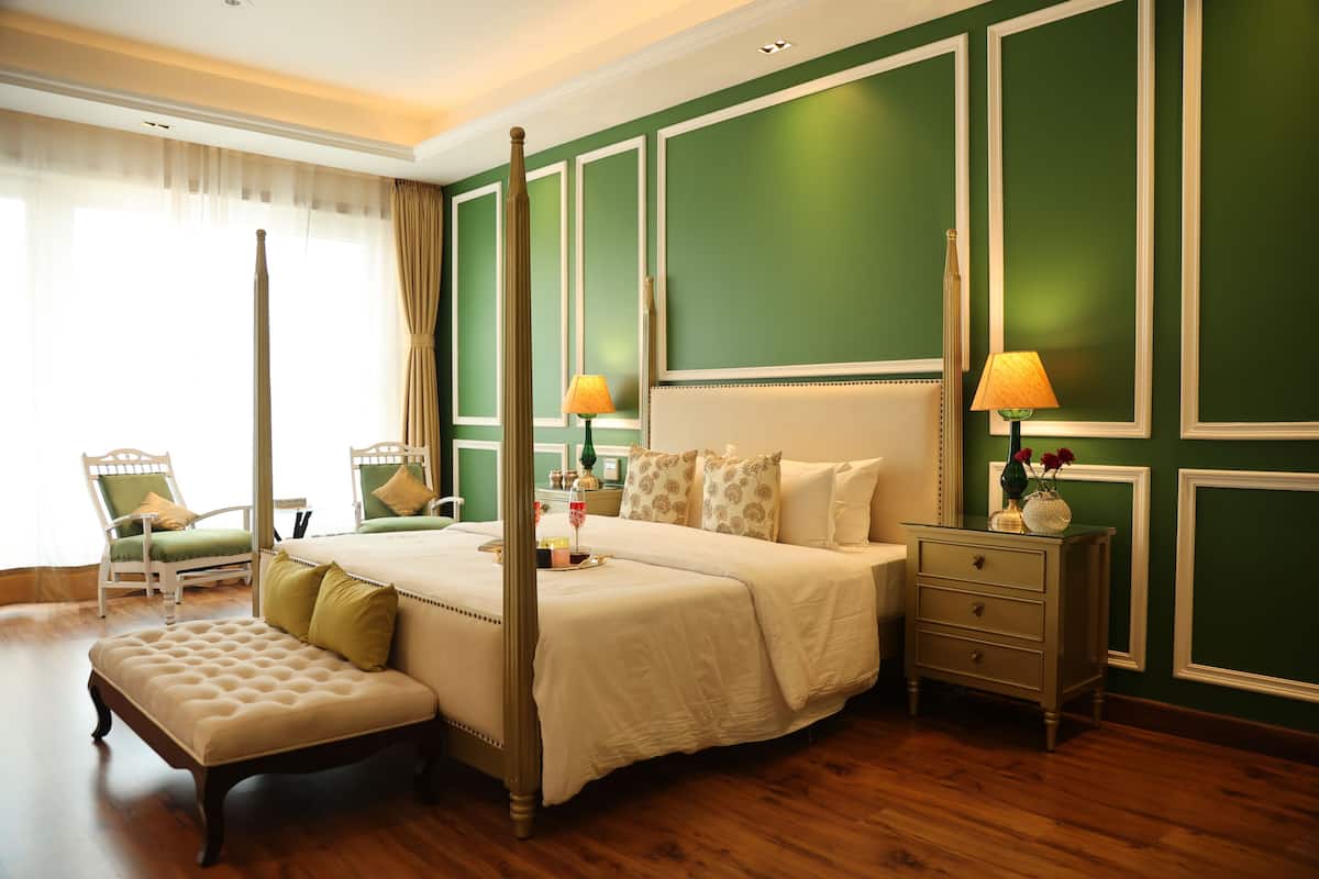 A four-poster bed with a footboard, a bedside table with a lamp, a bench, and a chair with a cushion.
