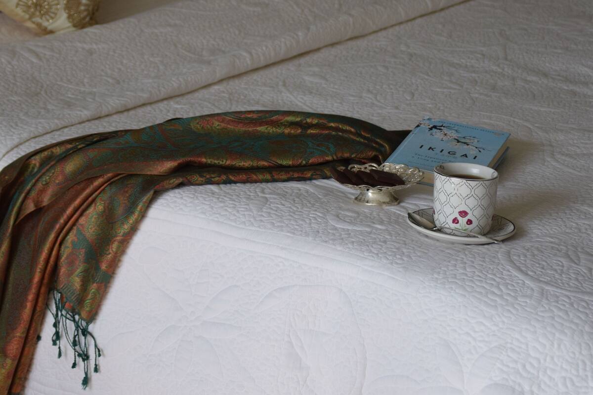 A neatly made bed with patterned pillows, a decorative throw, and a small table with a teacup and a book.