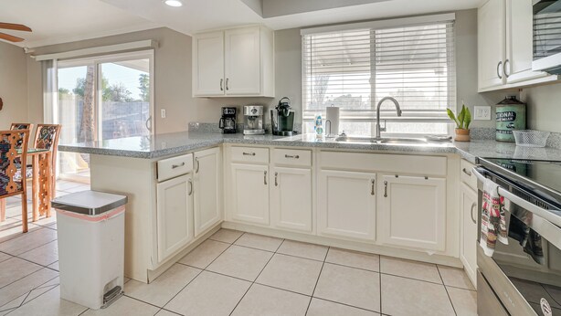 A modern kitchen with white cabinets, a granite countertop, a built-in oven, and a window with blinds. - 8 Mi to State Farm Stadium: Glendale Home w/ Grill (Peoria)