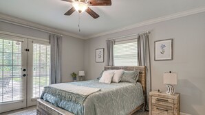 Une chambre à coucher avec un lit, une table de chevet en bois, un ventilateur de plafond et une porte avec des stores.