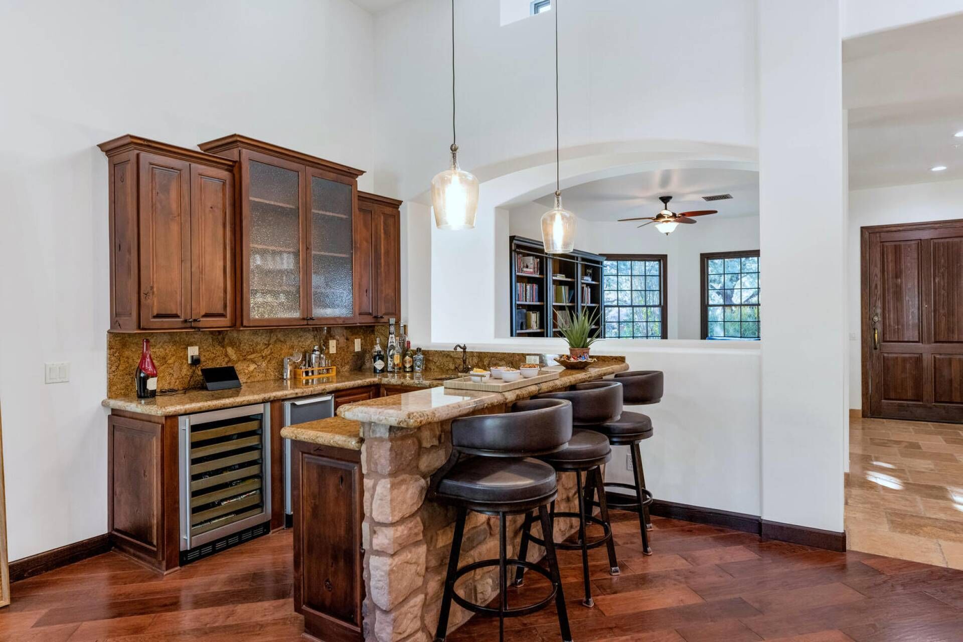 A kitchen with a stone island, bar stools, wooden cabinets, and a ceiling fan.