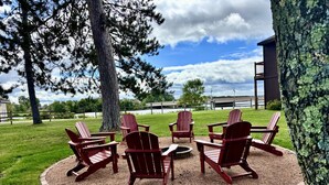 A circular outdoor seating area with Adirondack chairs and a fire pit, surrounded by a gravel path and grass. - Every Room with a Beautiful View of The Wisconsin River * (Tomahawk)