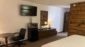 A hotel room with a bed, a desk with a chair, a television, a wooden dresser, and a wooden wall panel. - Every Room with a Beautiful View of The Wisconsin River * (Tomahawk)