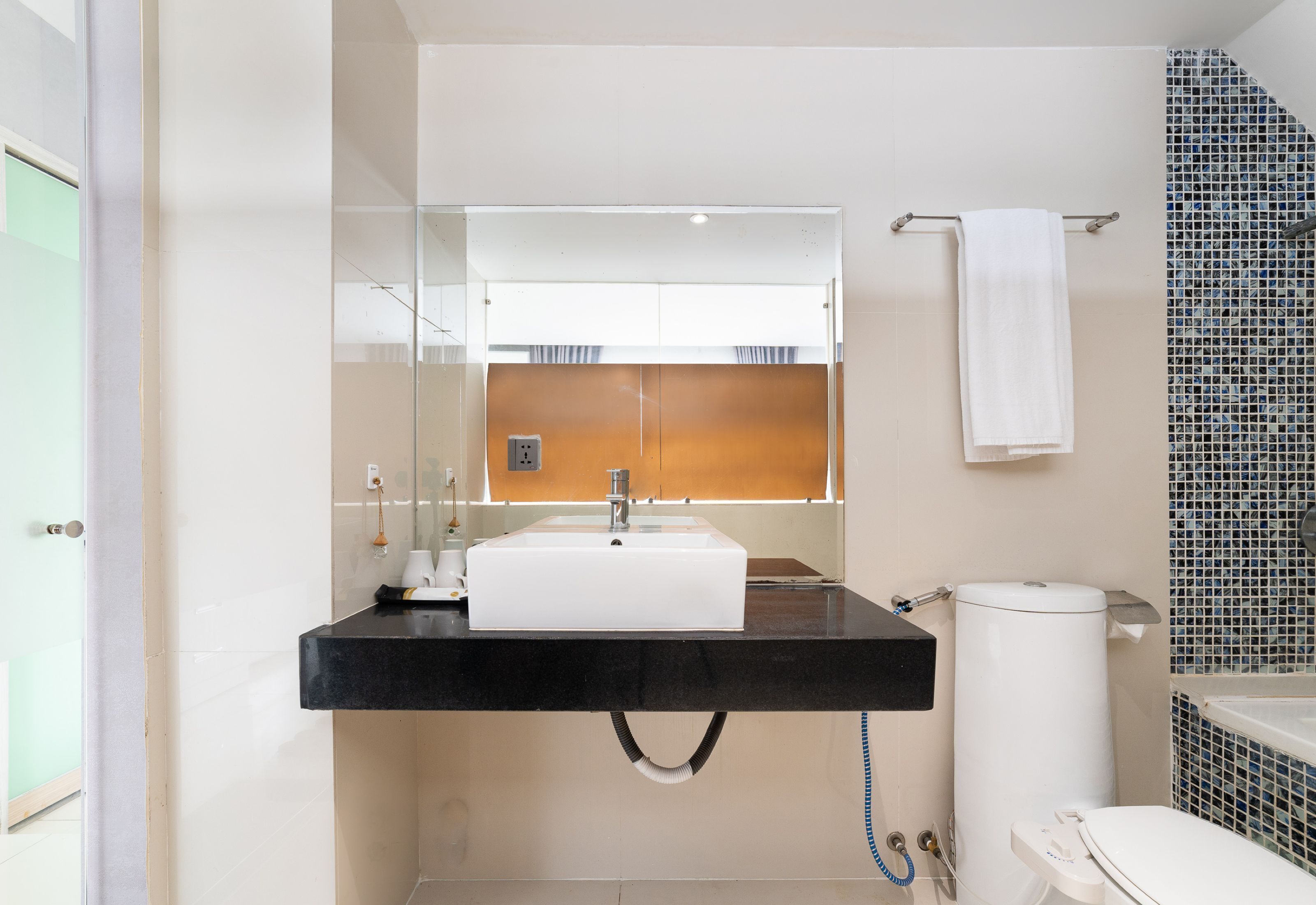 Une salle de bain moderne avec un lavabo noir, un miroir, des toilettes blanches et un espace douche avec un mur carrelé.