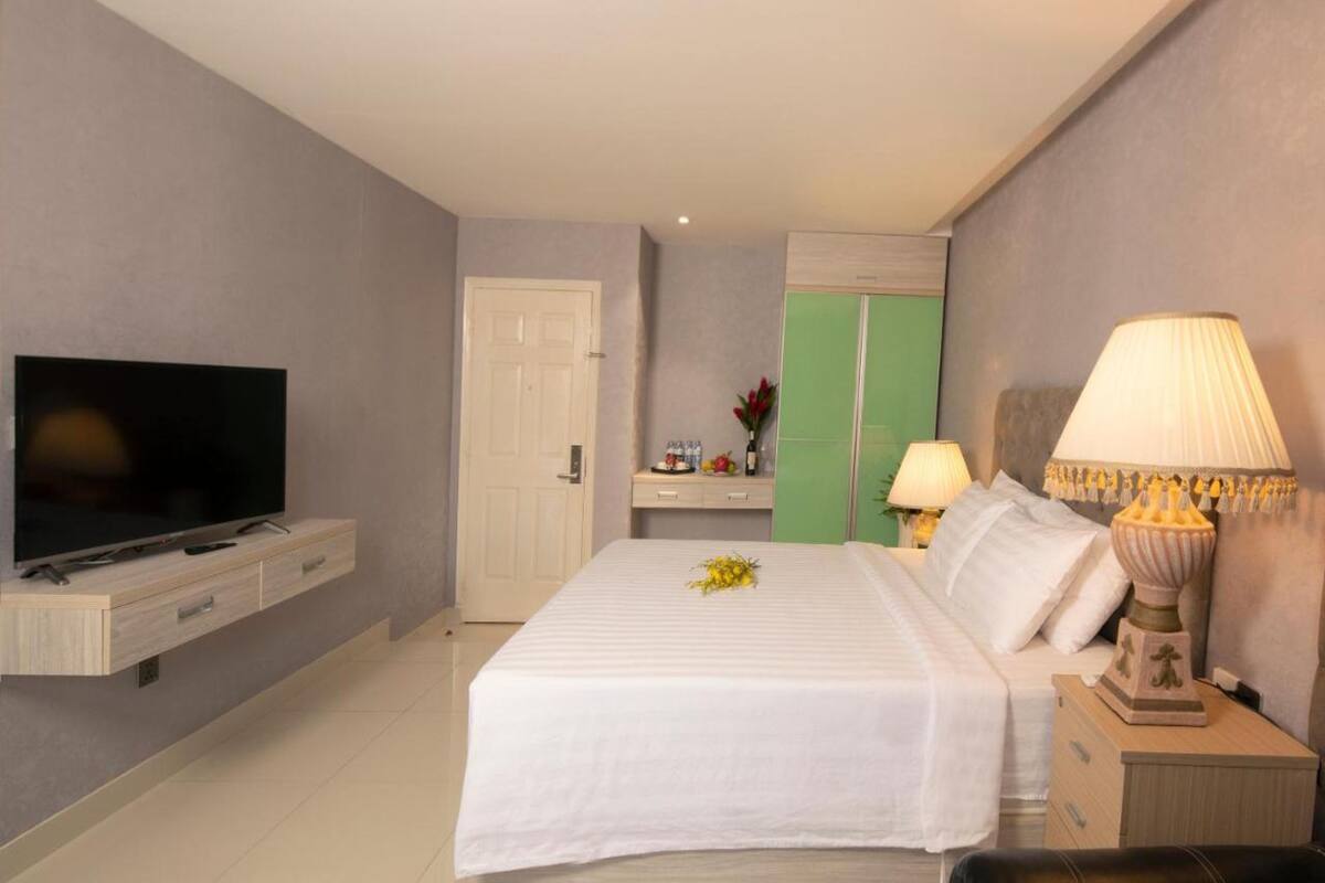 A hotel room with a bed, a television on a wooden console, a bedside table with a lamp, and a green wardrobe.