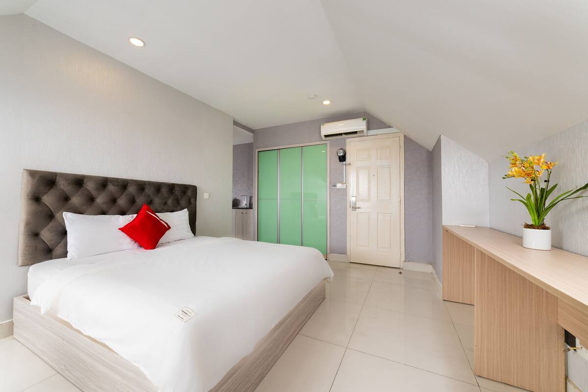 A modern hotel room with a large bed, a desk, a green wardrobe, and a white door.