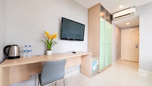A modern hotel room with a wooden desk, a flat-screen TV, a potted plant, and a minibar.