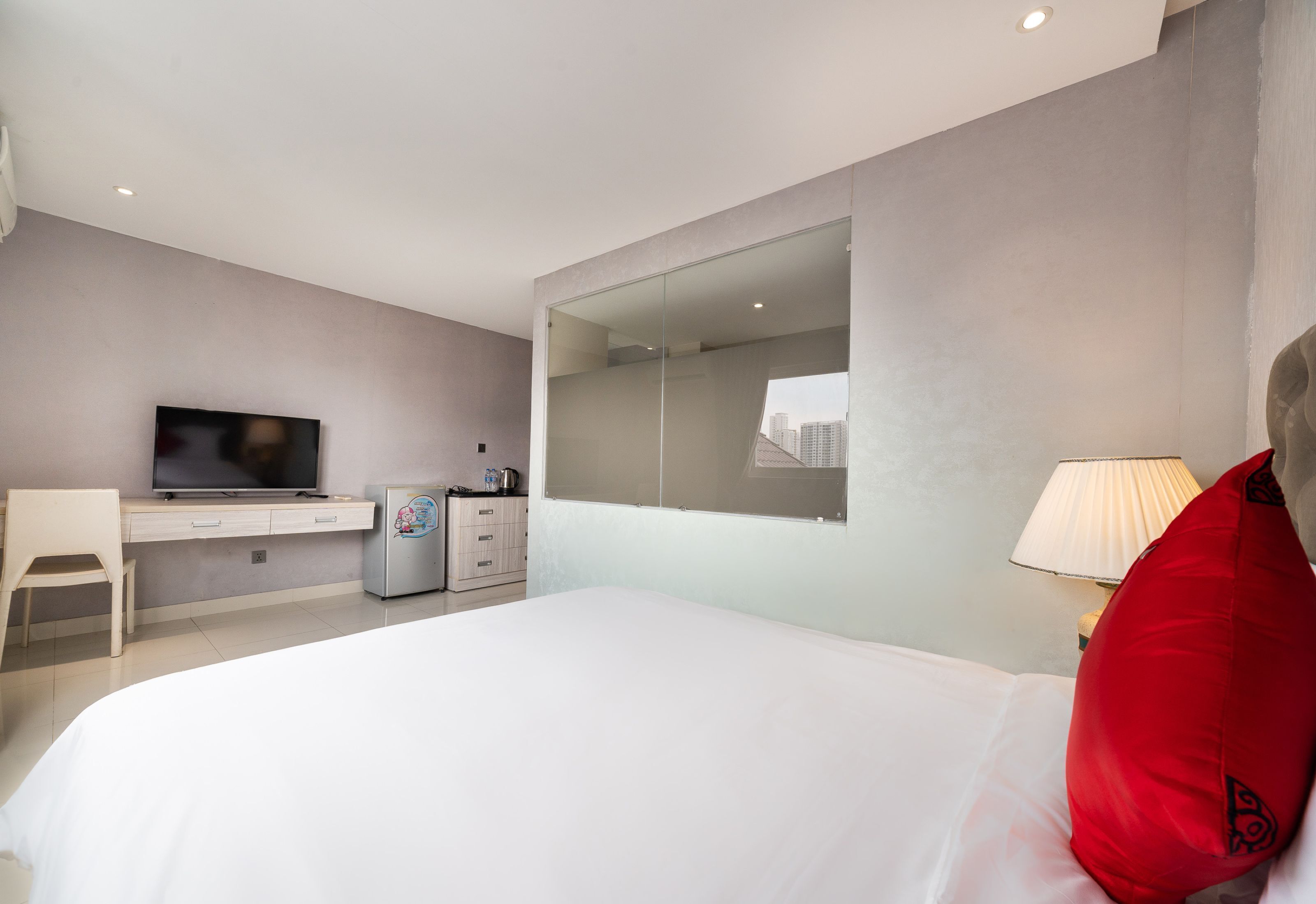 A modern hotel room with a large bed, a desk, a television, a refrigerator, and a mirror.