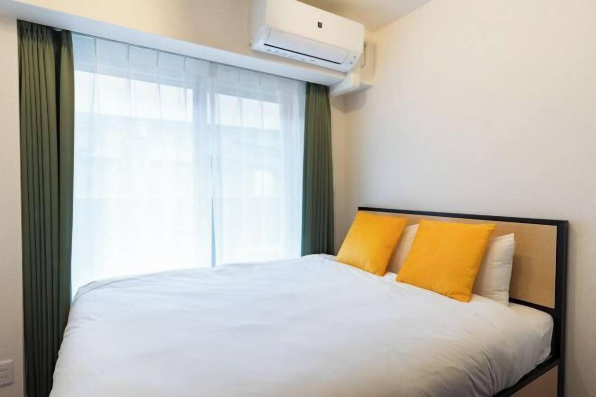 A hotel room with a bed, air conditioning unit, and a window with curtains.
