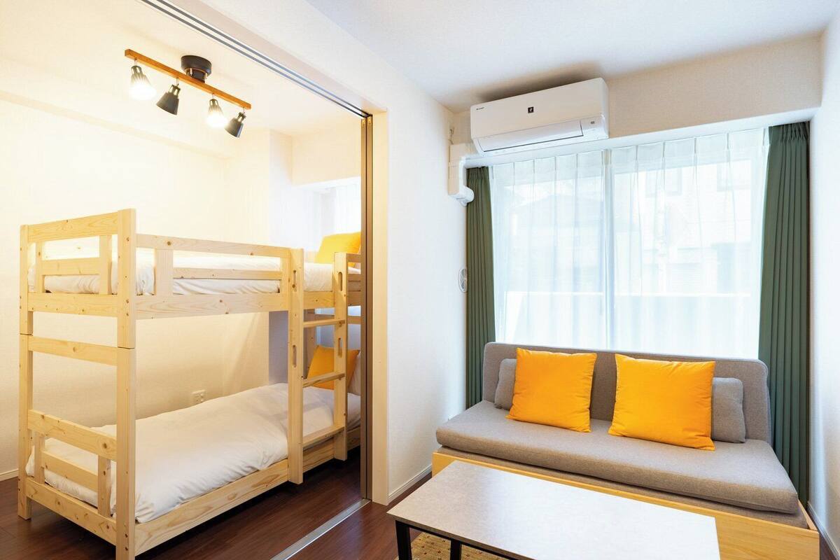 A room with bunk beds, a sofa with cushions, a table, and an air conditioning unit.