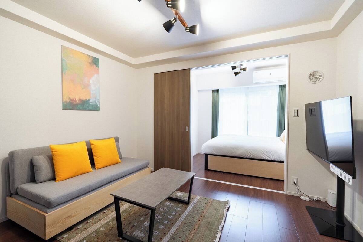 A modern hotel room with a sofa, a bed, a TV, and a painting on the wall.