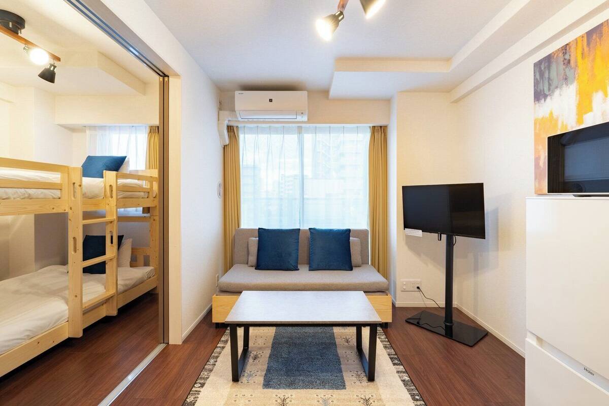 A compact hotel room with bunk beds, a sofa, a TV, and an air conditioning unit.