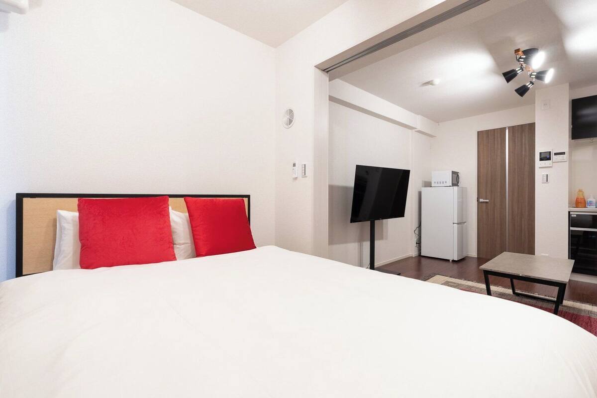 A hotel room with a bed, a TV, a refrigerator, and a small kitchen area.