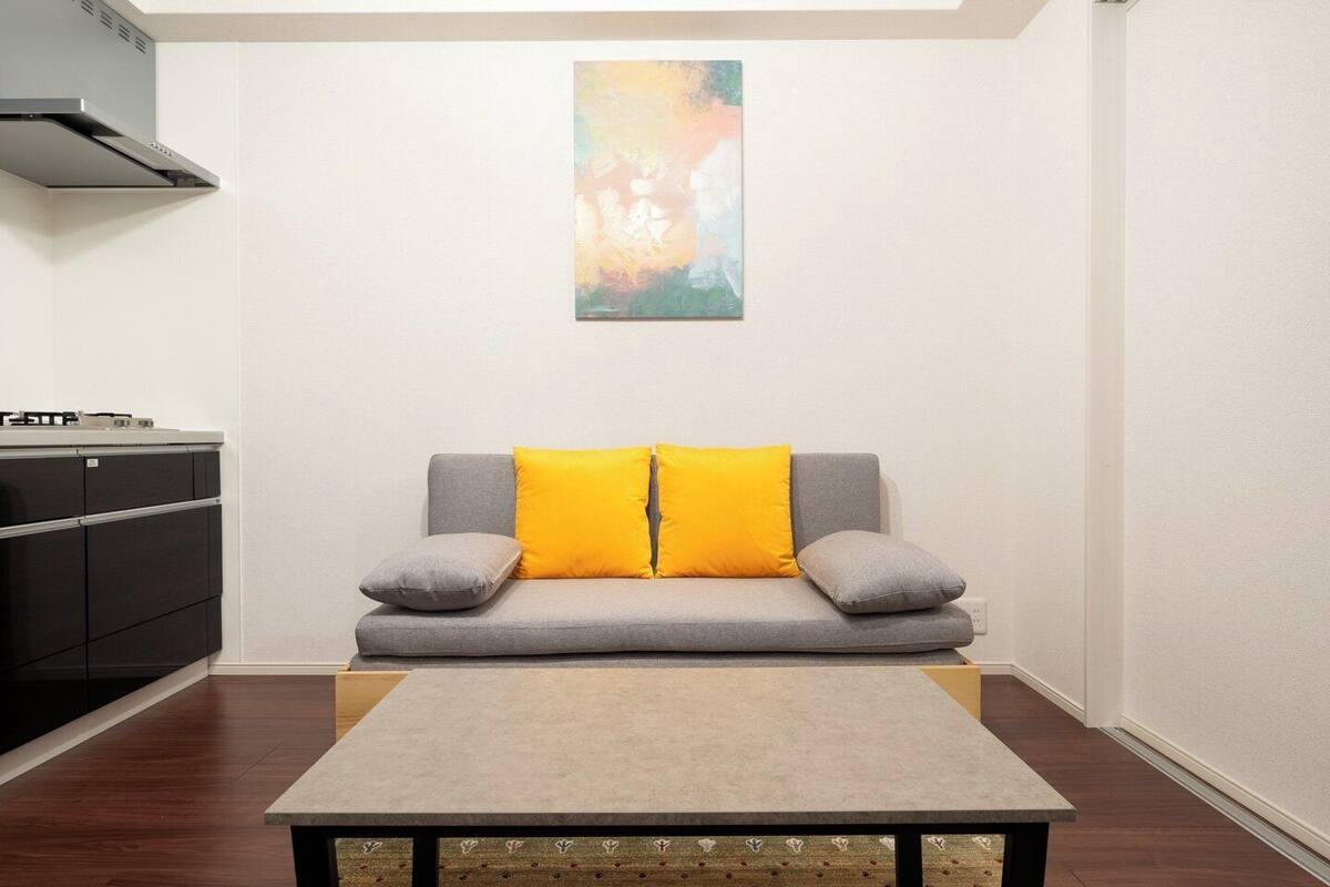 A modern living room with a grey sofa, two yellow cushions, a grey table, and a black cabinet.