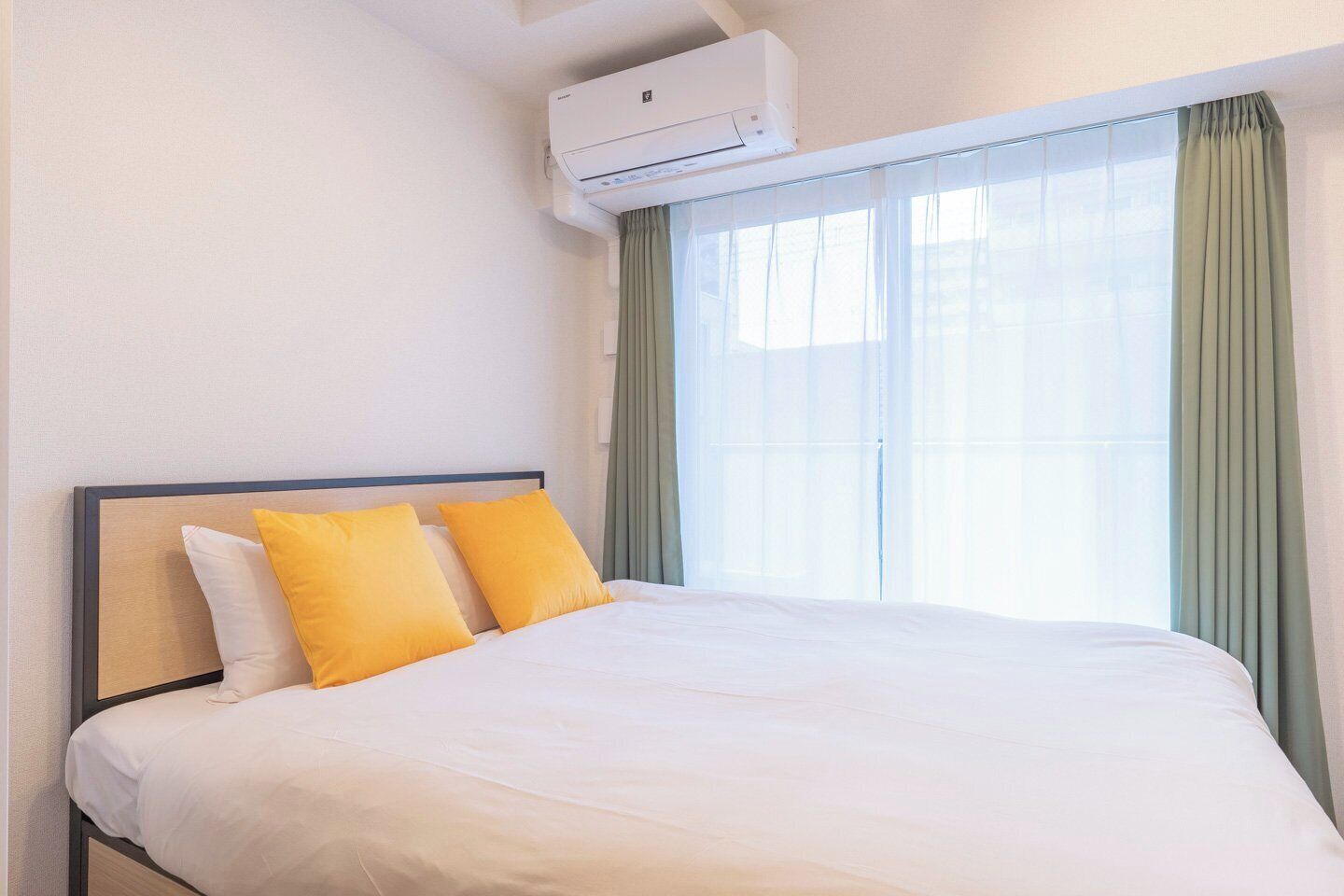 Quarto de hotel com cama, ar condicionado e uma janela grande com cortinas.