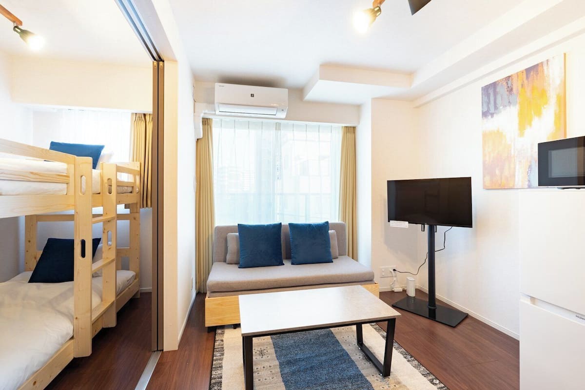 A compact hotel room with bunk beds, a sofa with blue cushions, a flat-screen TV, and a small table.