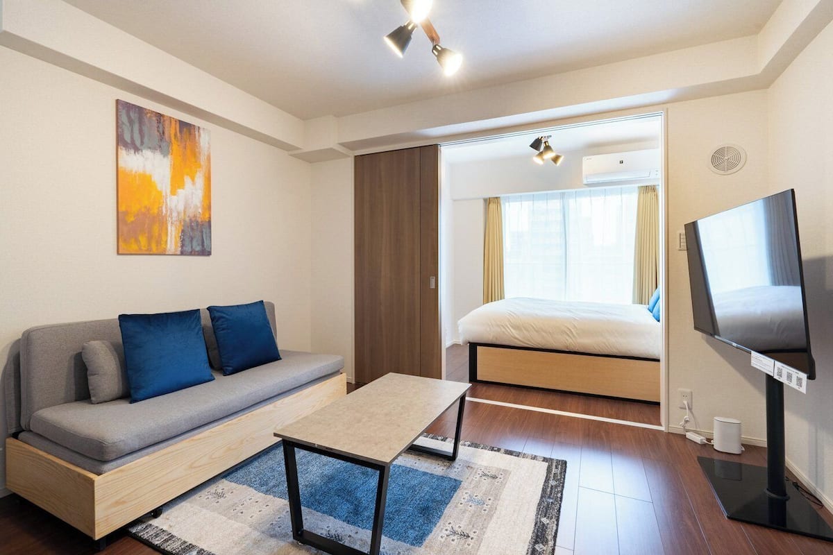 A modern hotel room with a sofa, a bed, a TV, and a painting on the wall.