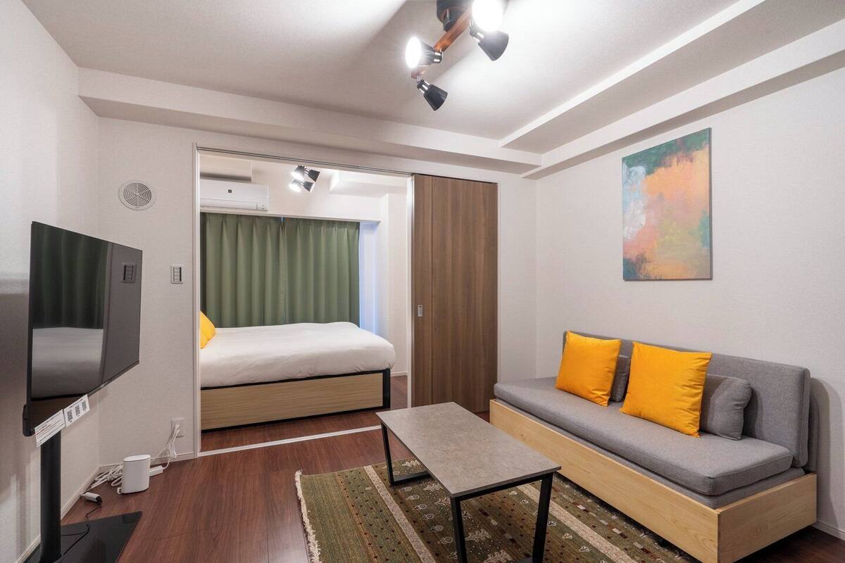 A compact hotel room with a bed, a sofa, a TV, and a painting on the wall.