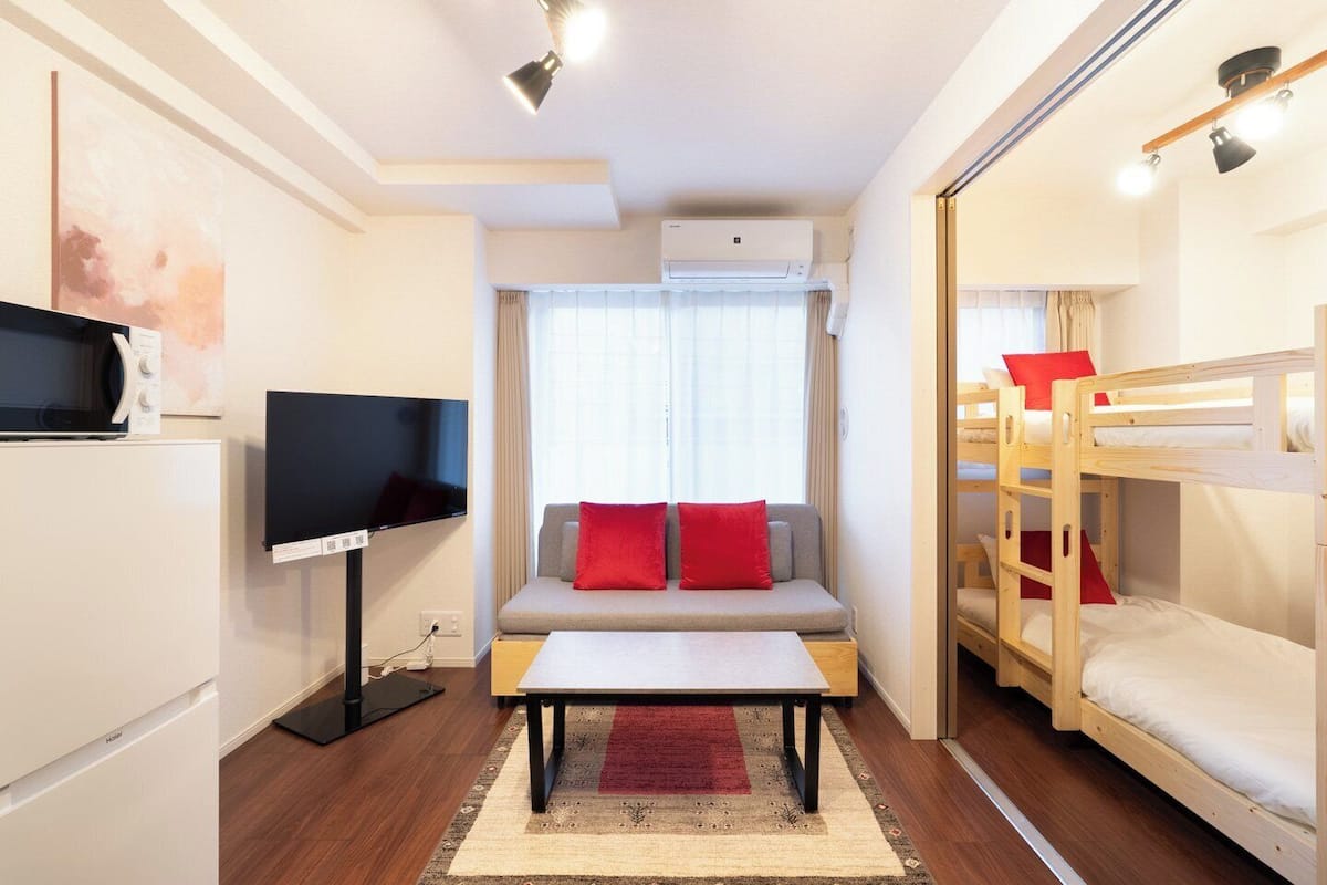 A compact hotel room with a sofa, a TV, bunk beds, and a microwave.