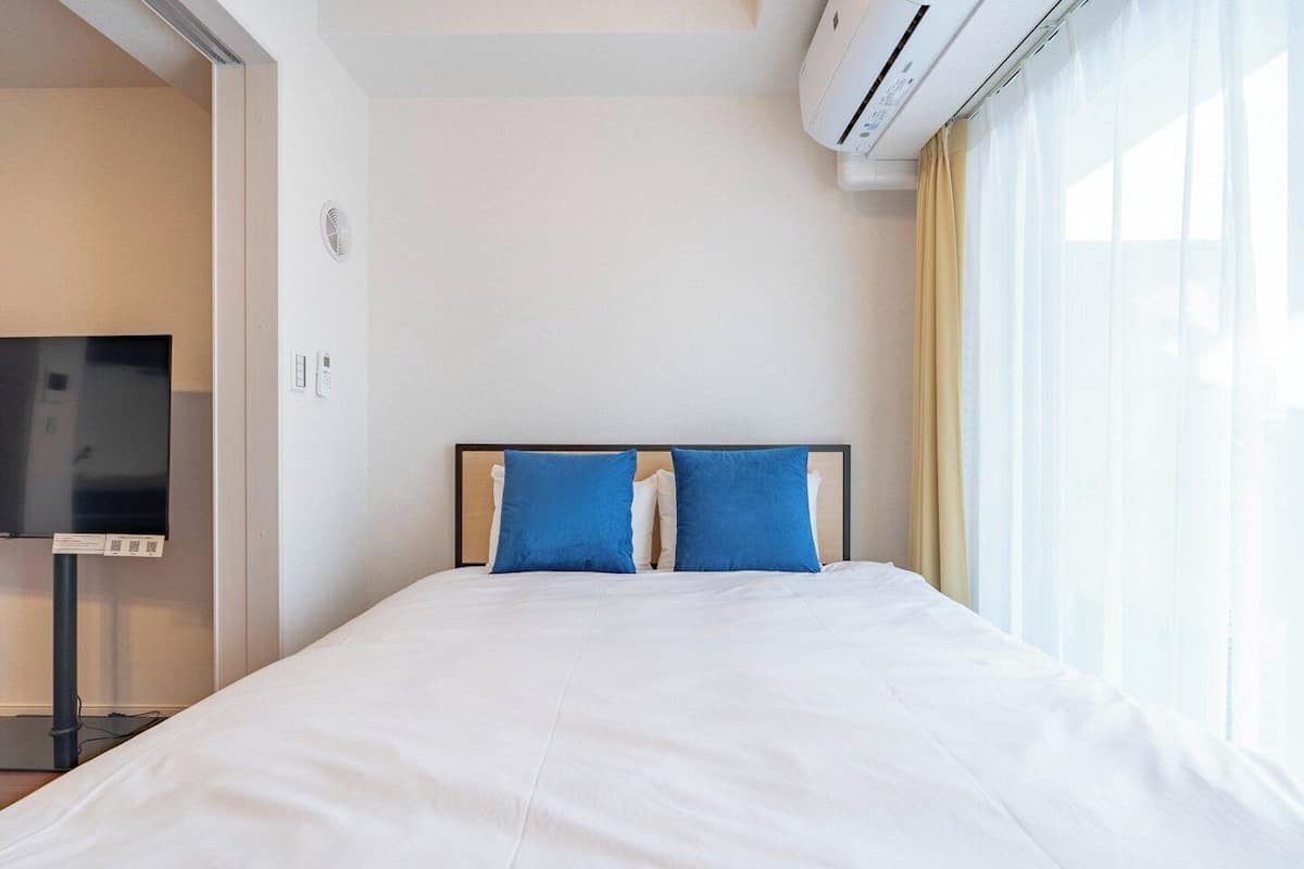 A hotel room with a bed, a TV, an air conditioning unit, and a window with curtains.