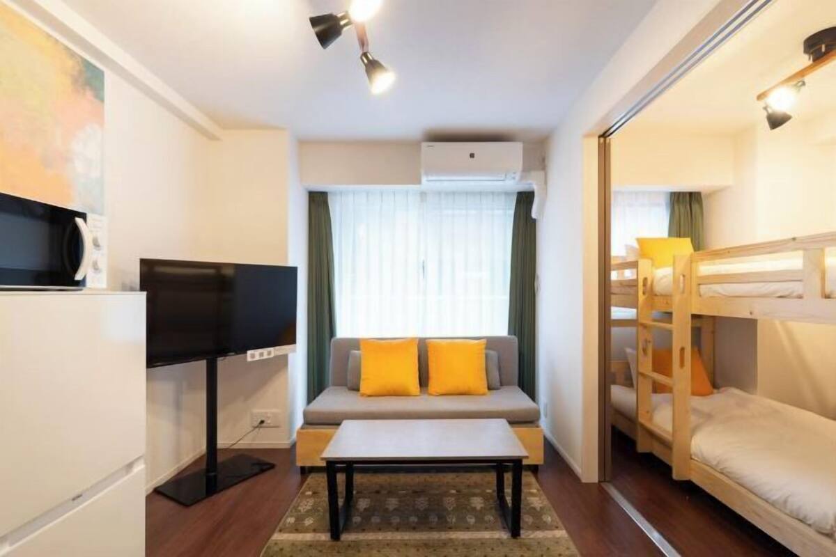 A compact room with a sofa, a television, a bunk bed, and a small table.