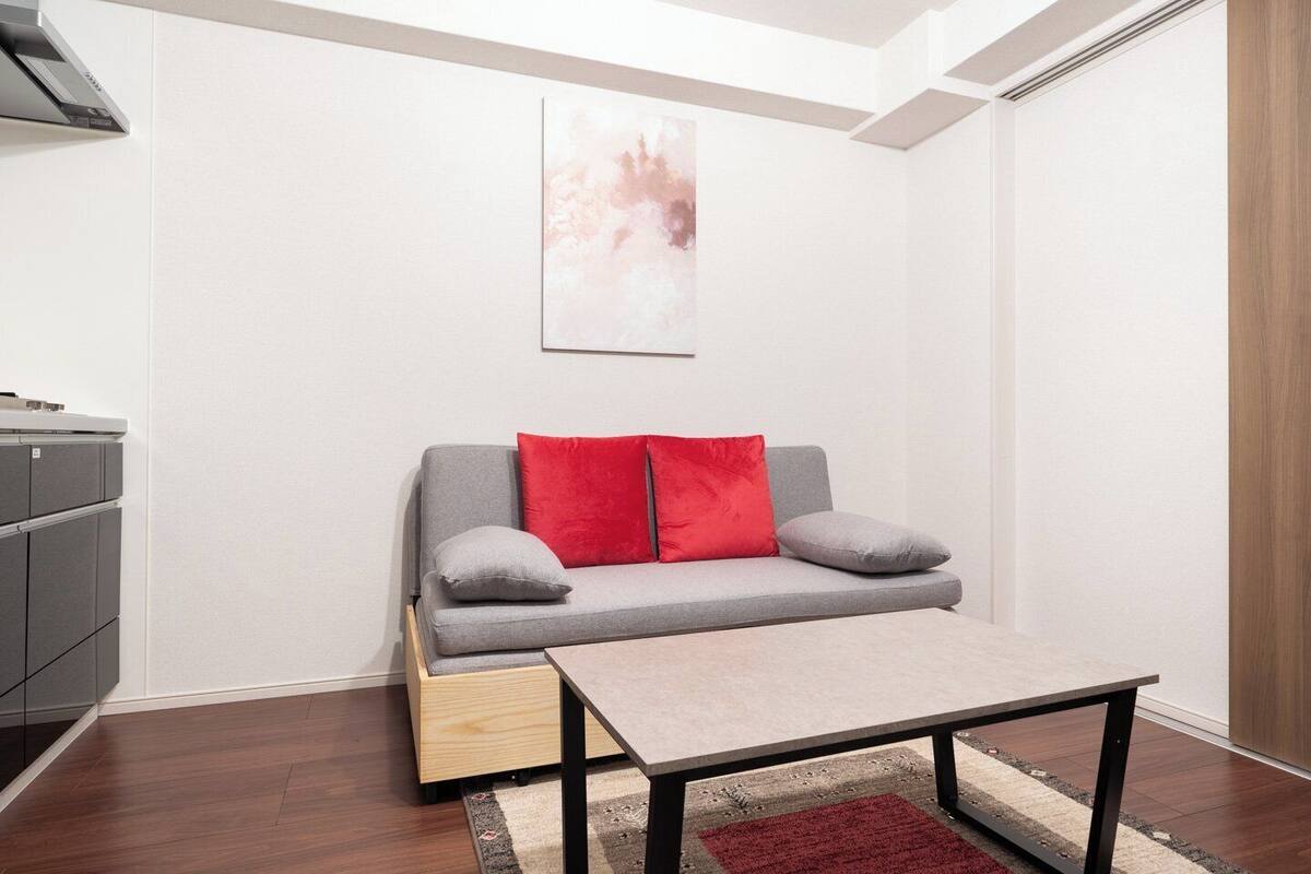 A compact living space with a grey sofa, red and grey cushions, a small wooden table, and a red rug.