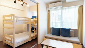 A room with a bunk bed, a sofa, a table, and an air conditioning unit. - MAT OSAKA NAGARA (Osaka)