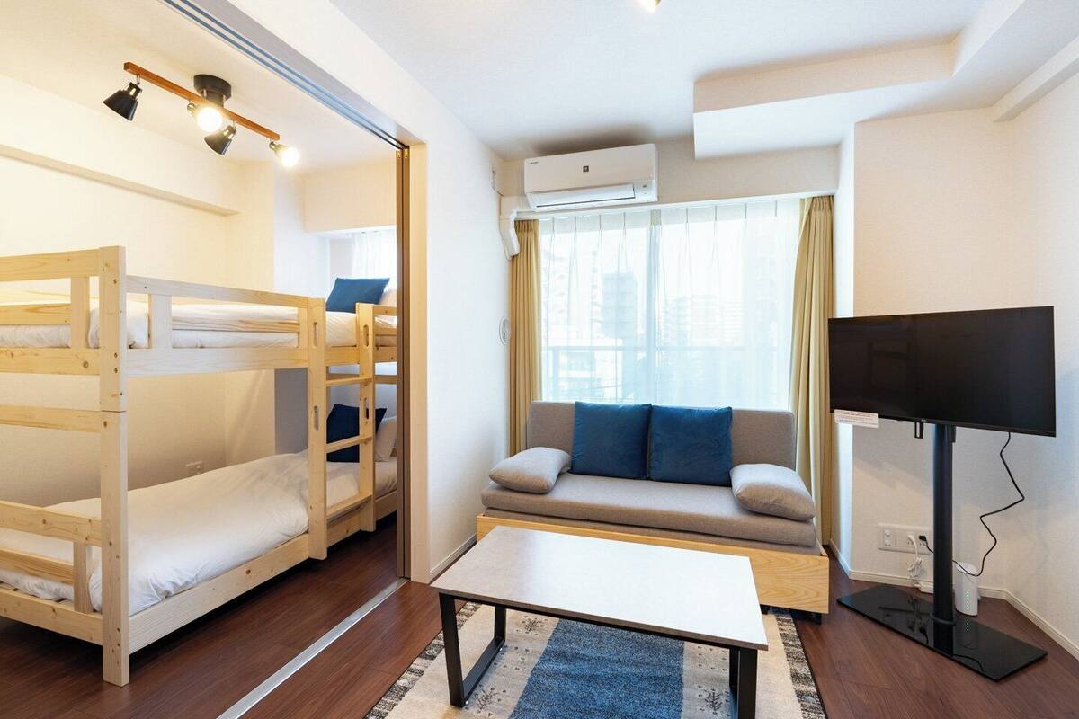 A room with bunk beds, a sofa, a TV, and an air conditioning unit.