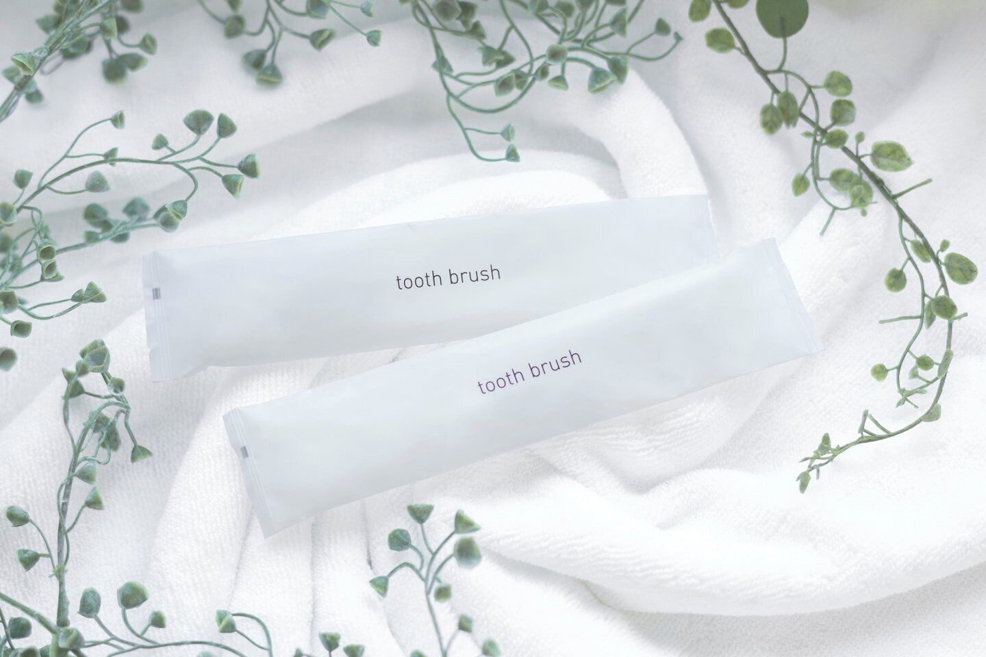 Two white tubes labeled 'tooth brush' on a white fabric background with green foliage.