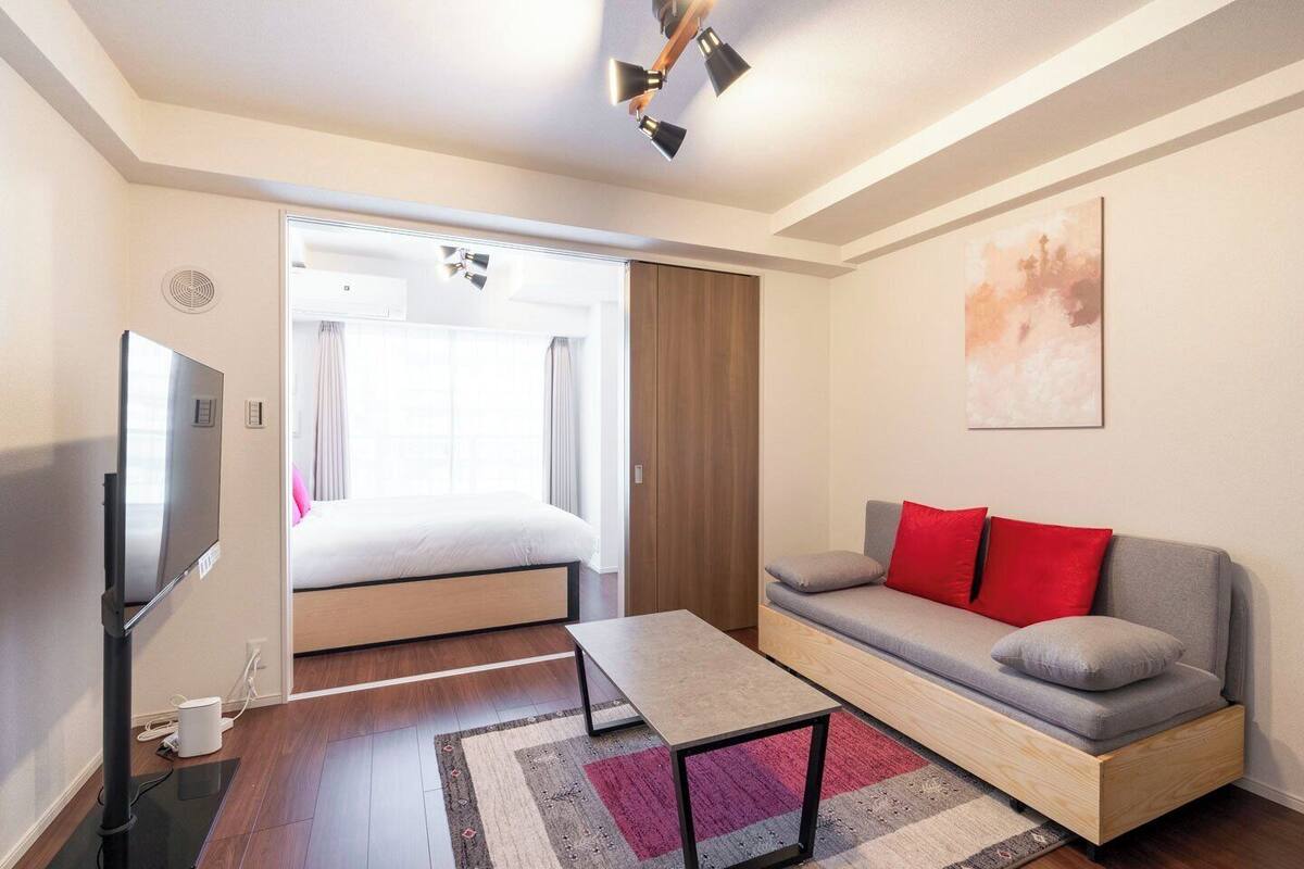 A modern hotel room with a bed, a sofa, a TV, and a ceiling fan.