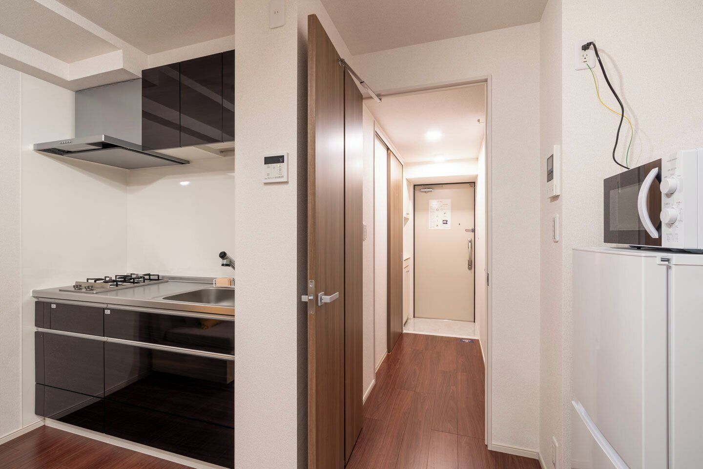 A compact kitchen with a stove, sink, and cabinets, a wooden door, and a microwave on a white cabinet.