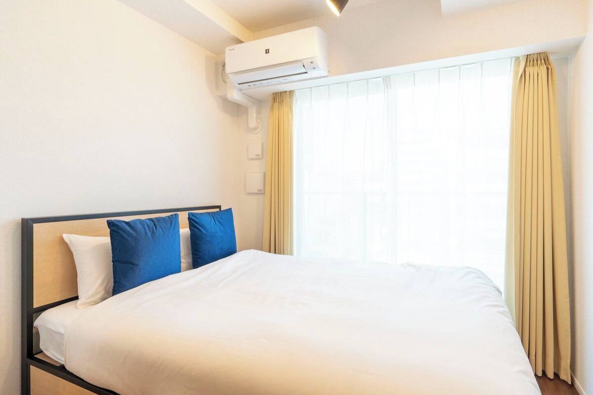 A hotel room with a bed, a window with curtains, and an air conditioning unit.