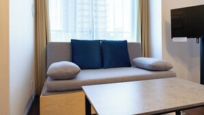 A modern hotel room with a sofa, two pillows, a small table, and a TV on the wall. - MAT OSAKA NAGARA (Osaka)